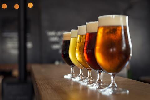 Glasses with different types of beer lined up on a bar.